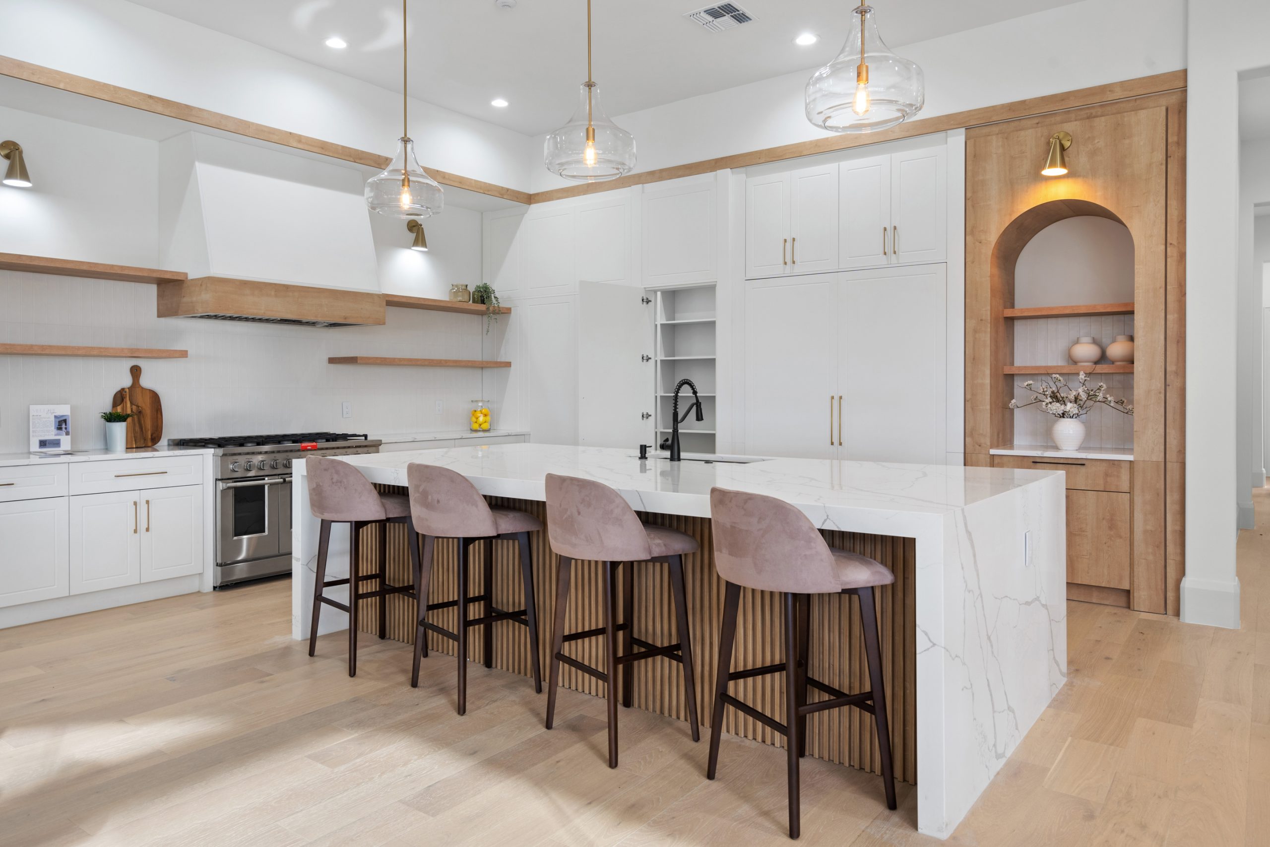 Cozinha americana com ilha em casa nos estados unidos, de alto padrão, integrada com varanda, living e área gourmet. Cozinha branca com detalhes amadeirados e formas orgânicas. Puxadores cromados. Móveis planejados cozinha