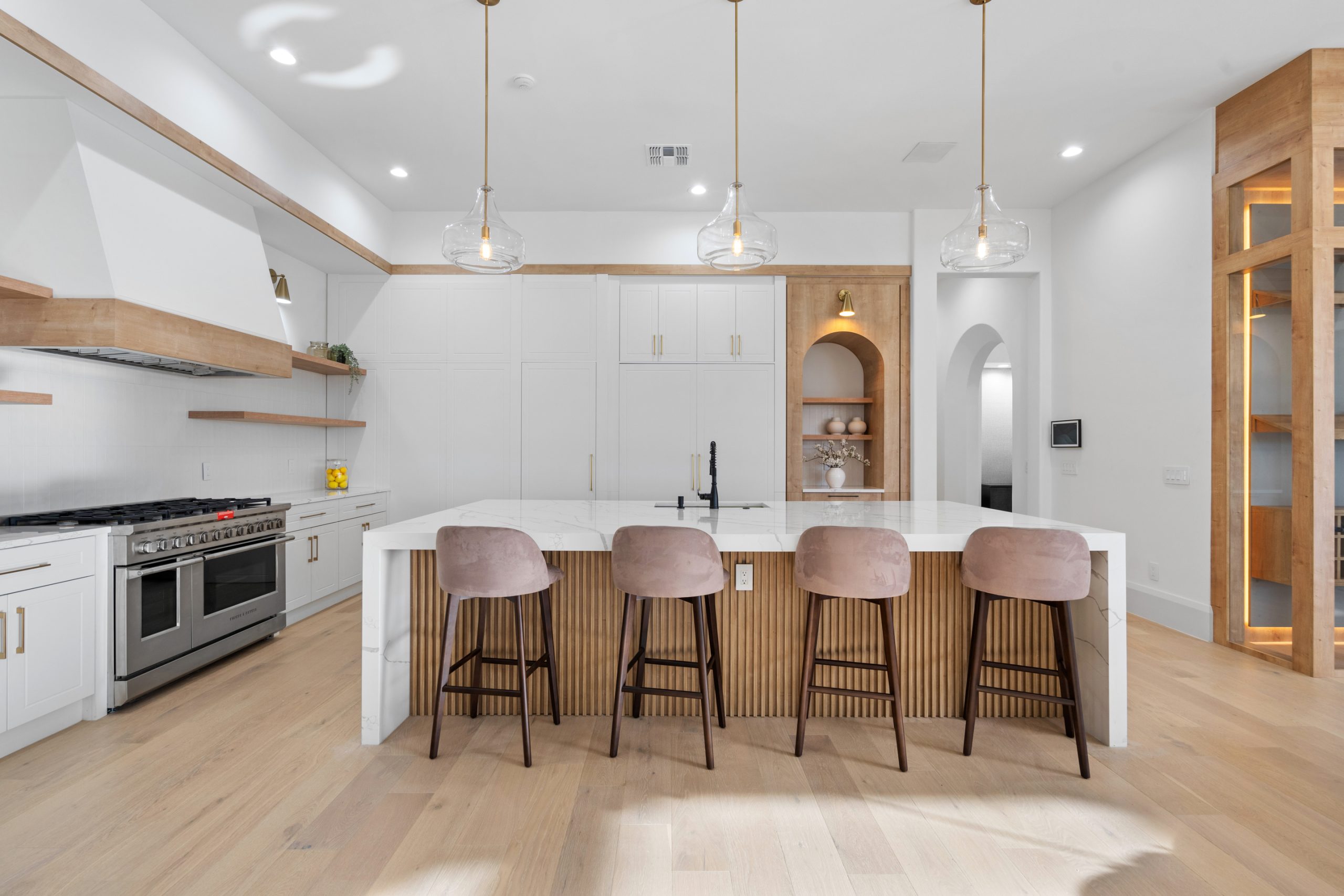 Cozinha americana com ilha em casa nos estados unidos, de alto padrão, integrada com varanda, living e área gourmet. Cozinha branca com detalhes amadeirados e formas orgânicas. Puxadores cromados.