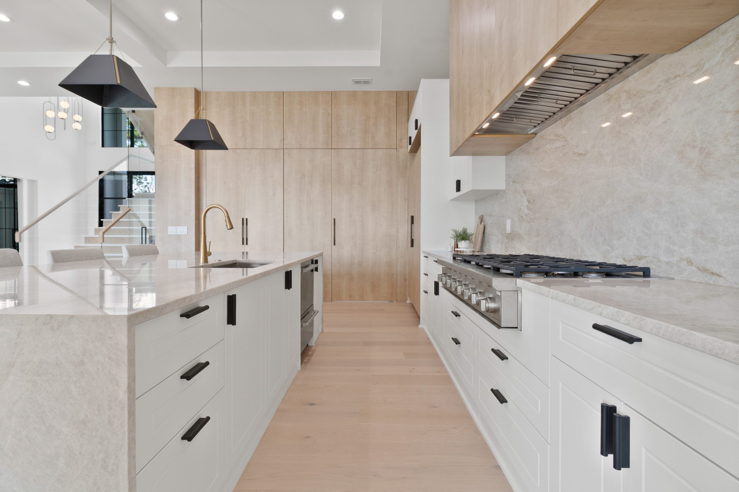 Cozinha americana em casa nos estados unidos, de alto padrão, integrada com varanda, living e área gourmet. Cozinha branca com detalhes amadeirados. Puxadores pretos. Cloud Dancer Pantone com madeira e pedra