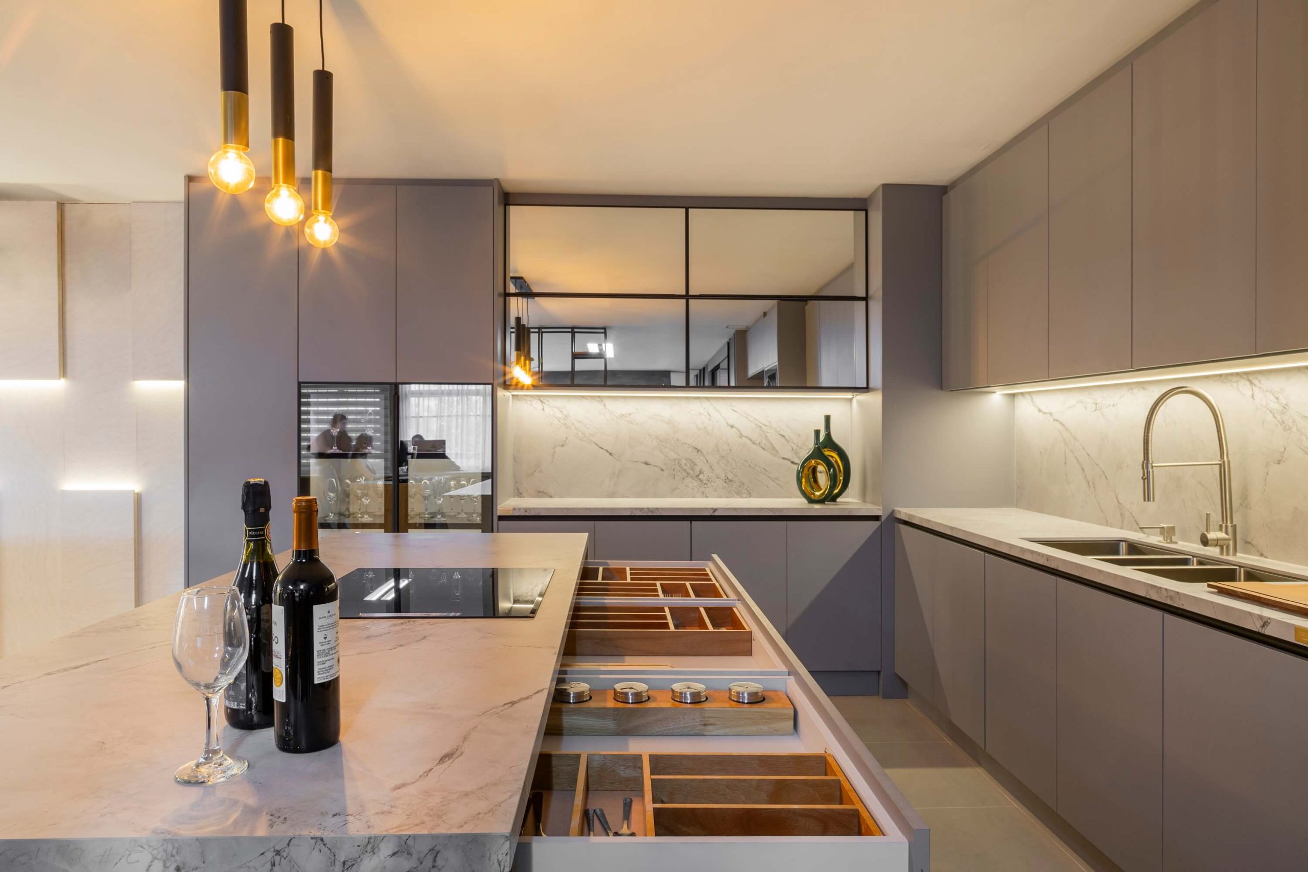 Cozinha de luxo, com gavetas abertas na ilha para mostrar os divisores de madeira para organização dos talheres, temperos e utensílios da cozinha. A cozinha é em tons de cinza, com detalhes em portas de vidro