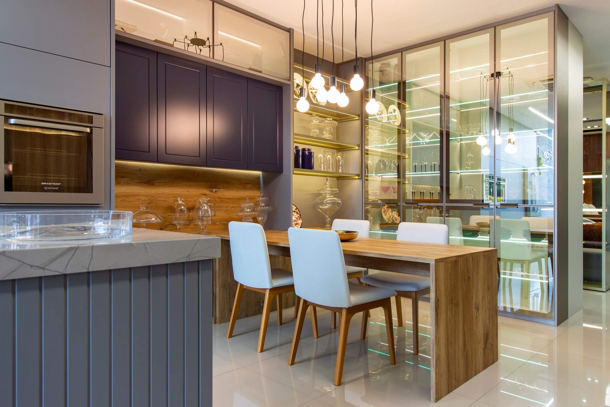Cozinha Contemporânea com Ilha em tom de cinza e azul escuro, com cristaleira alta de luxo com portas de vidro translúcidas. bancada de refeições para 4 pessoas. - Móveis planejados cozinha