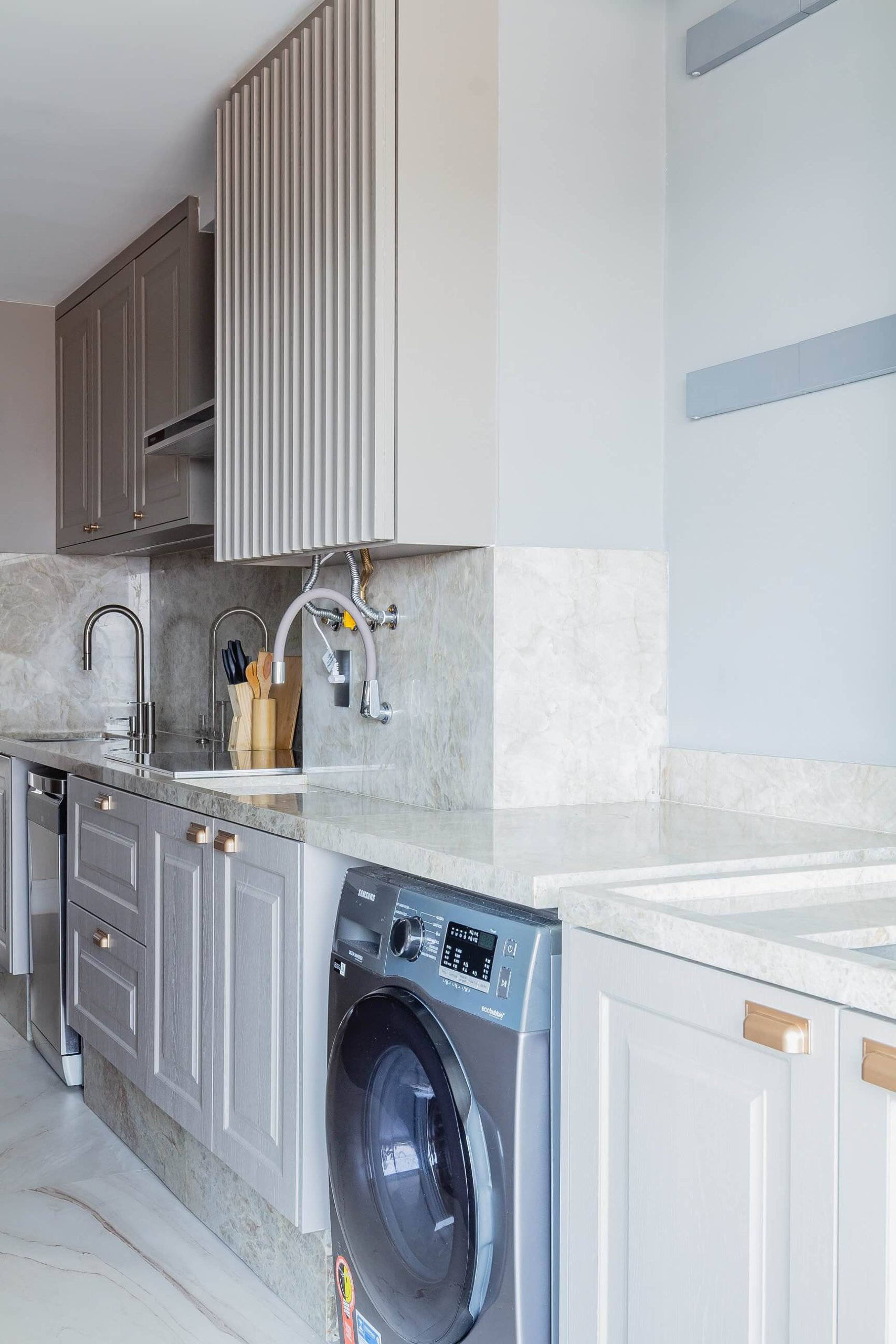 Detalhe de uma lavanderia integrada a cozinha, onde a máquina de lavar está embutida na marcenaria com móvel para o tanque ao lado.