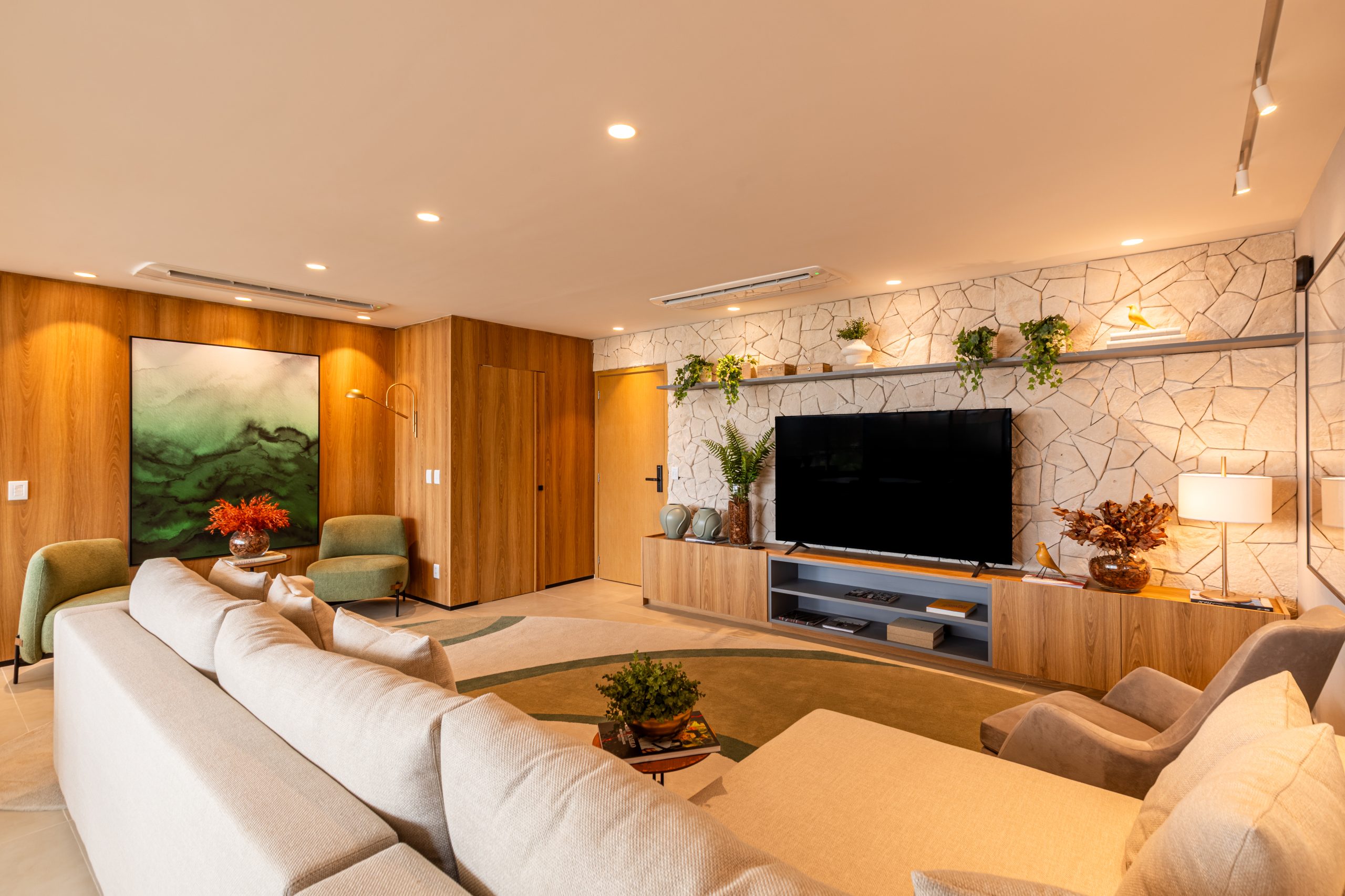 Living - sala de estar aconchegante com pegada de design natural, utilização de pedra na parede, marcenaria e mobiliário personalizado com revestimento de madeira nas paredes, decoração em tons neutros. Ambientes personalizados de alto padrão.