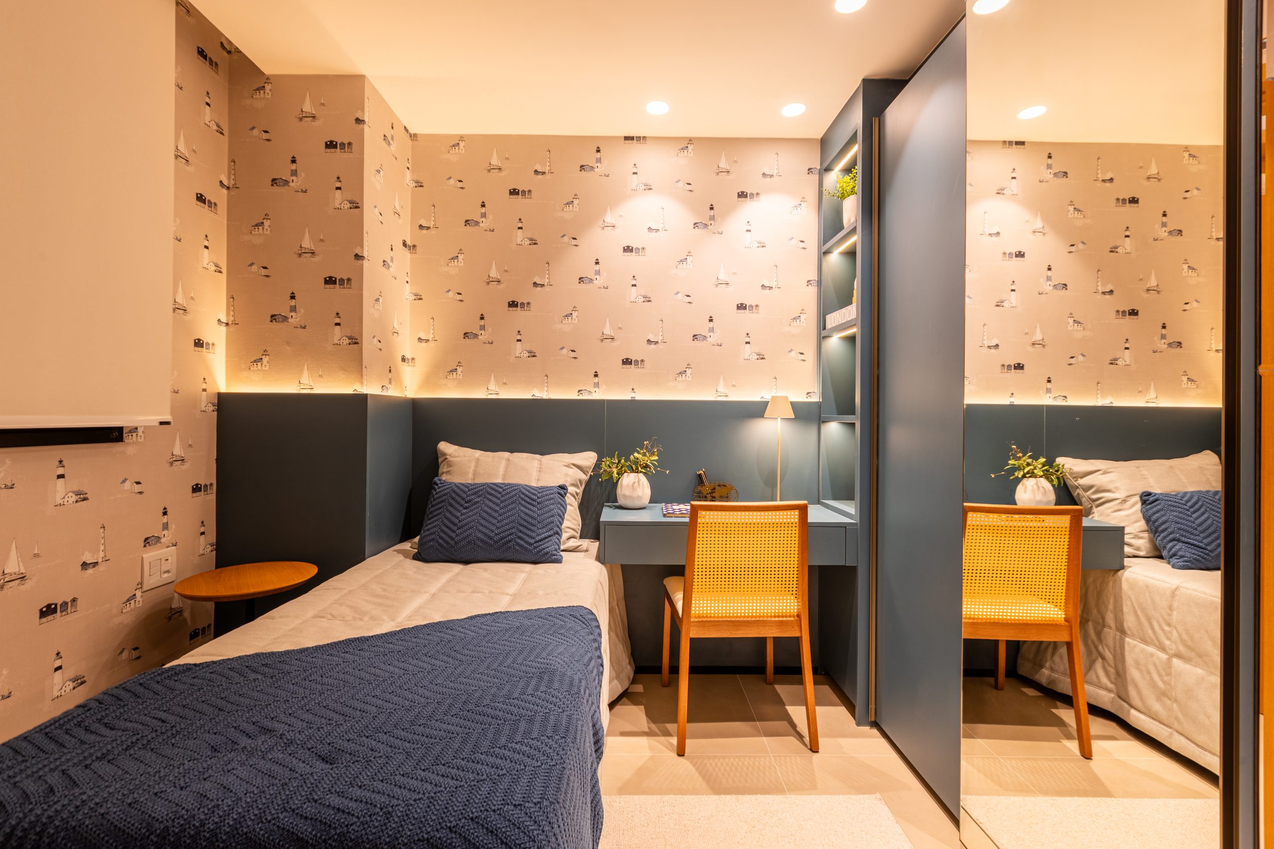 Dormitório jovem de menino em tons de azul com papel de parede delicado com grafismos de locais históricos, com área de estudo, nichos, roupeiro com porta de correr de espelho e cama de solteiro. cor do ano 2026