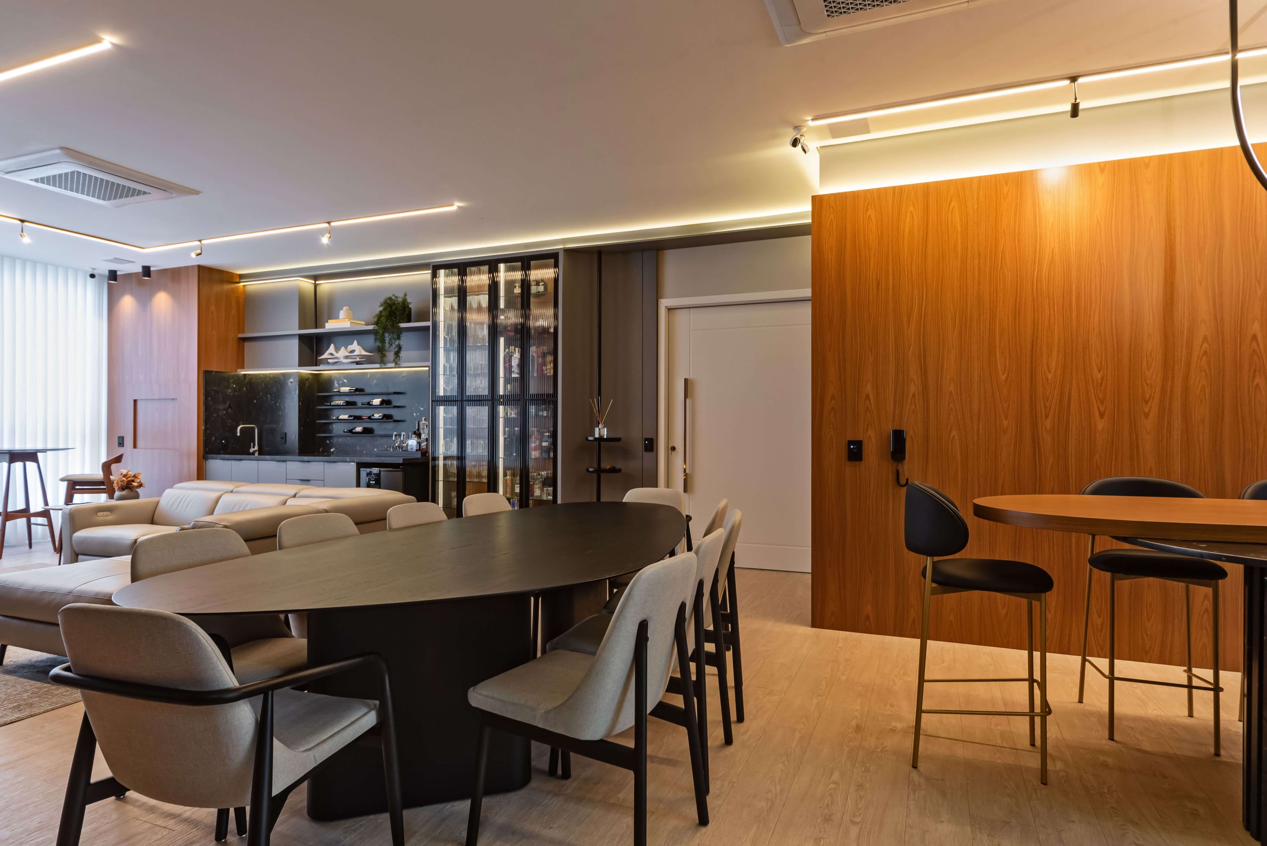 Ambiente gourmet Finger com integração entre cozinha e área social. Móveis planejados em tons neutros e texturas sofisticadas criam uma atmosfera elegante e acolhedora, perfeita para receber com conforto. SEO foco: ambiente gourmet planejado, integração de espaços, móveis Finger. Cozinha no tom cinza, mesa em mármore preto com pés ripados e living amplo no padrão freijó. Área do bar, adega e churrasqueira complementam o ambiente de estar.