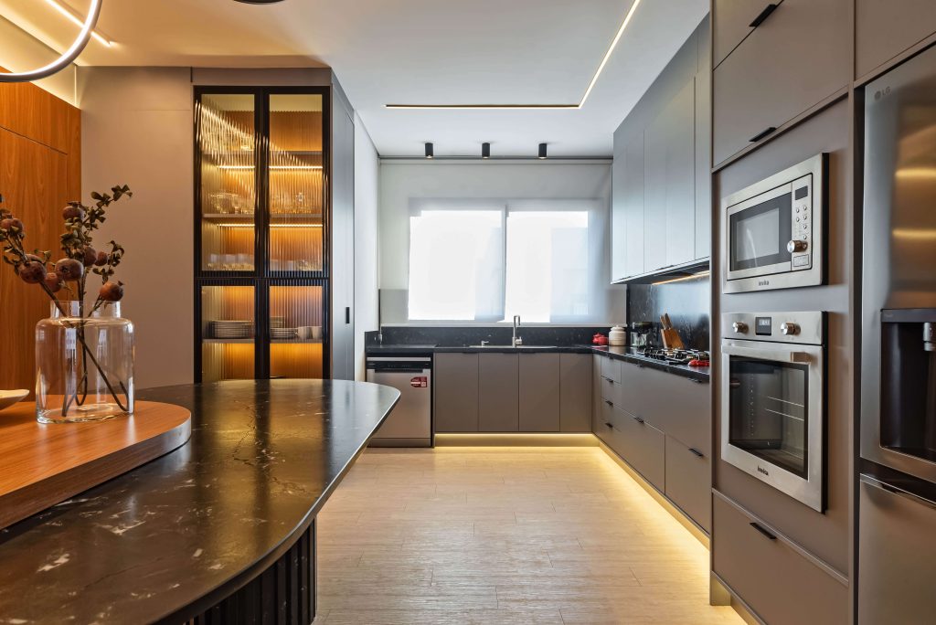 Ambiente gourmet Finger com integração entre cozinha e área social. Móveis planejados em tons neutros e texturas sofisticadas criam uma atmosfera elegante e acolhedora, perfeita para receber com conforto. SEO foco: ambiente gourmet planejado, integração de espaços, móveis Finger. Cozinha no tom cinza, mesa em mármore preto com pés ripados. Cristaleira com vidro canelado.