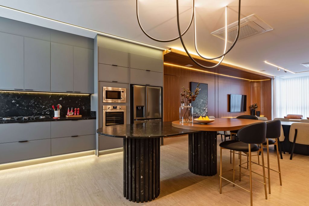 Ambiente gourmet Finger com integração entre cozinha e área social. Móveis planejados em tons neutros e texturas sofisticadas criam uma atmosfera elegante e acolhedora, perfeita para receber com conforto. SEO foco: ambiente gourmet planejado, integração de espaços, móveis Finger. Cozinha no tom cinza, mesa em mármore preto com pés ripados e living amplo no padrão freijó. Móveis planejados cozinha