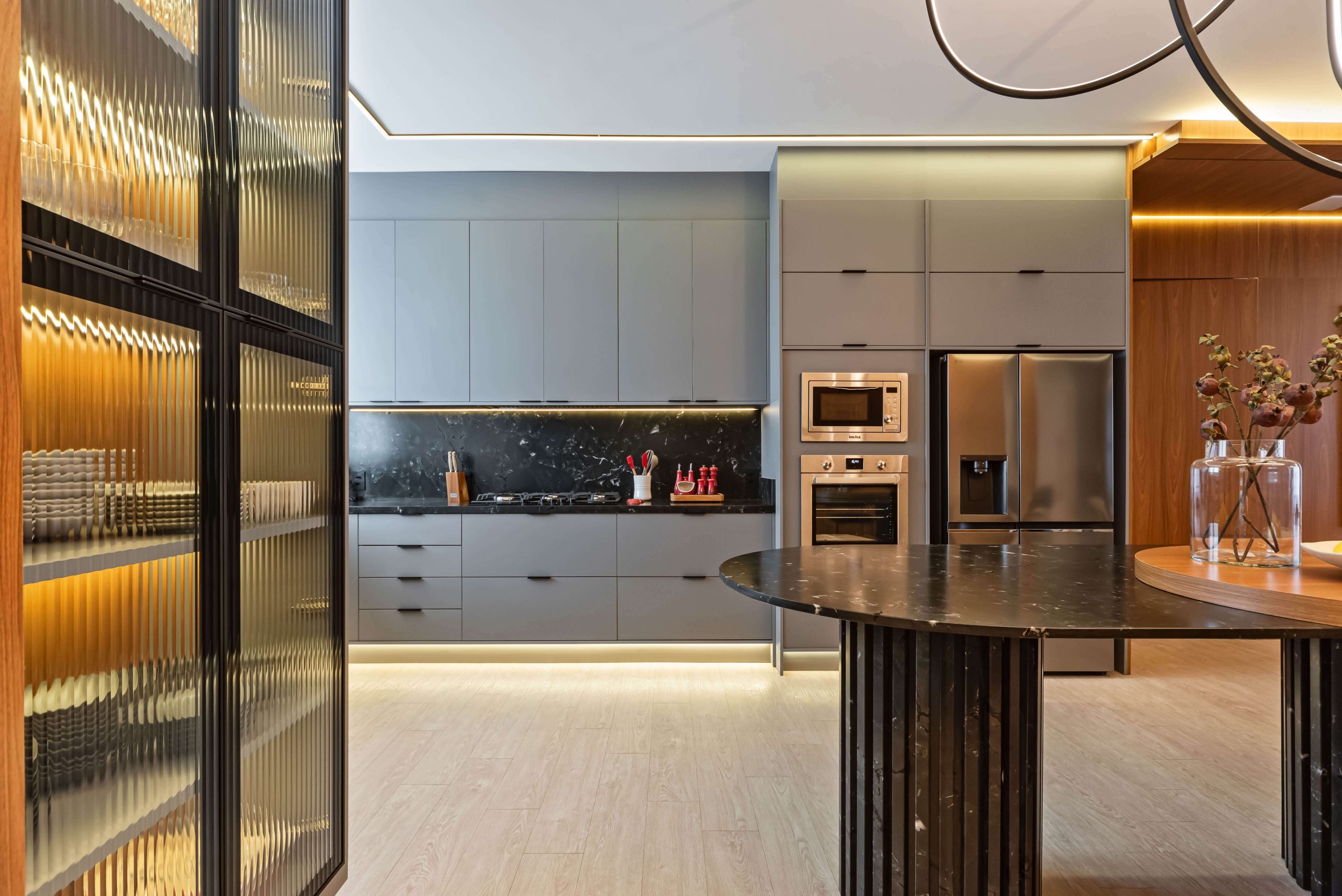 Ambiente gourmet Finger com integração entre cozinha e área social. Móveis planejados em tons neutros e texturas sofisticadas criam uma atmosfera elegante e acolhedora, perfeita para receber com conforto. SEO foco: ambiente gourmet planejado, integração de espaços, móveis Finger. Cozinha no tom cinza, mesa em mármore preto com pés ripados e living amplo no padrão freijó.