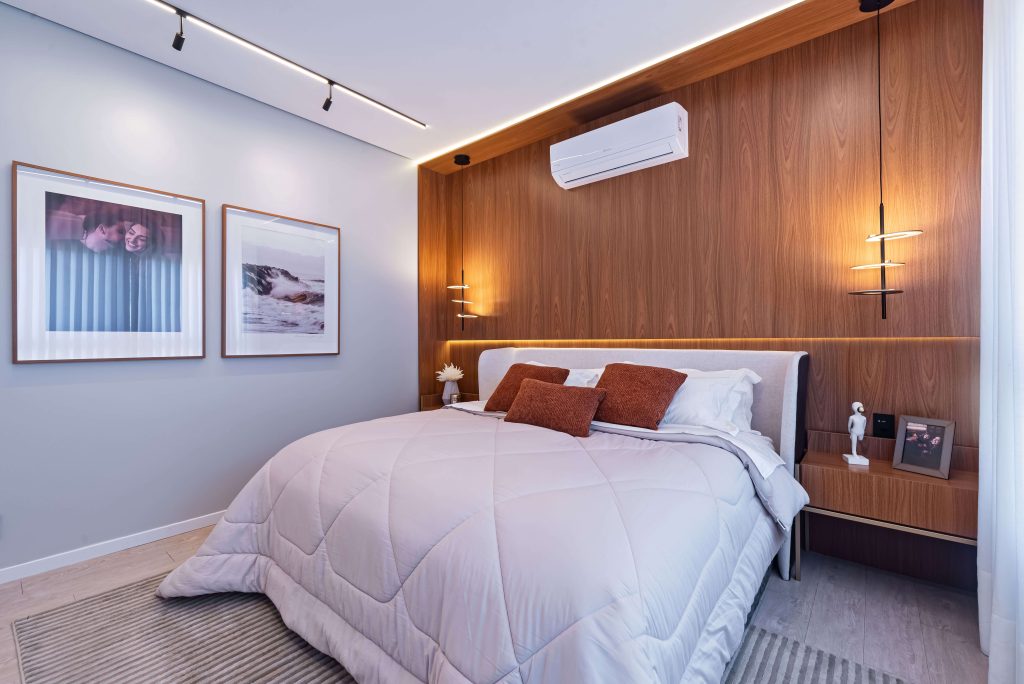 Suíte master do Casal, dormitório planejado de alto padrão, com cabeceira revestida em painel Freijó, uma madeira clássica e atemporal. A iluminação é indireta e ao lado da cama, duas mesas de cabeceira baixa que se camuflam com a cabeceira.