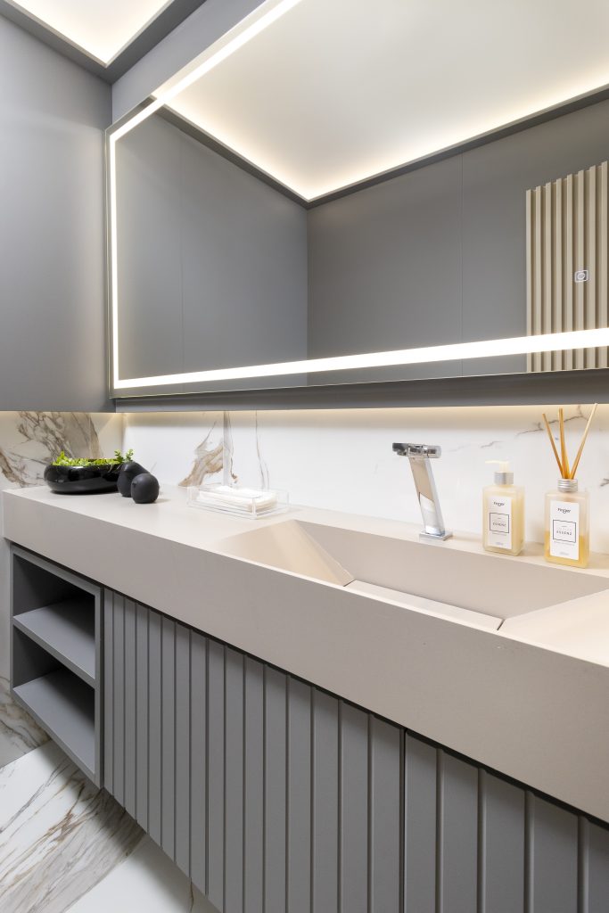 Banheiro cinza com espelho retroiluminado, portas ripadas da linha Lift