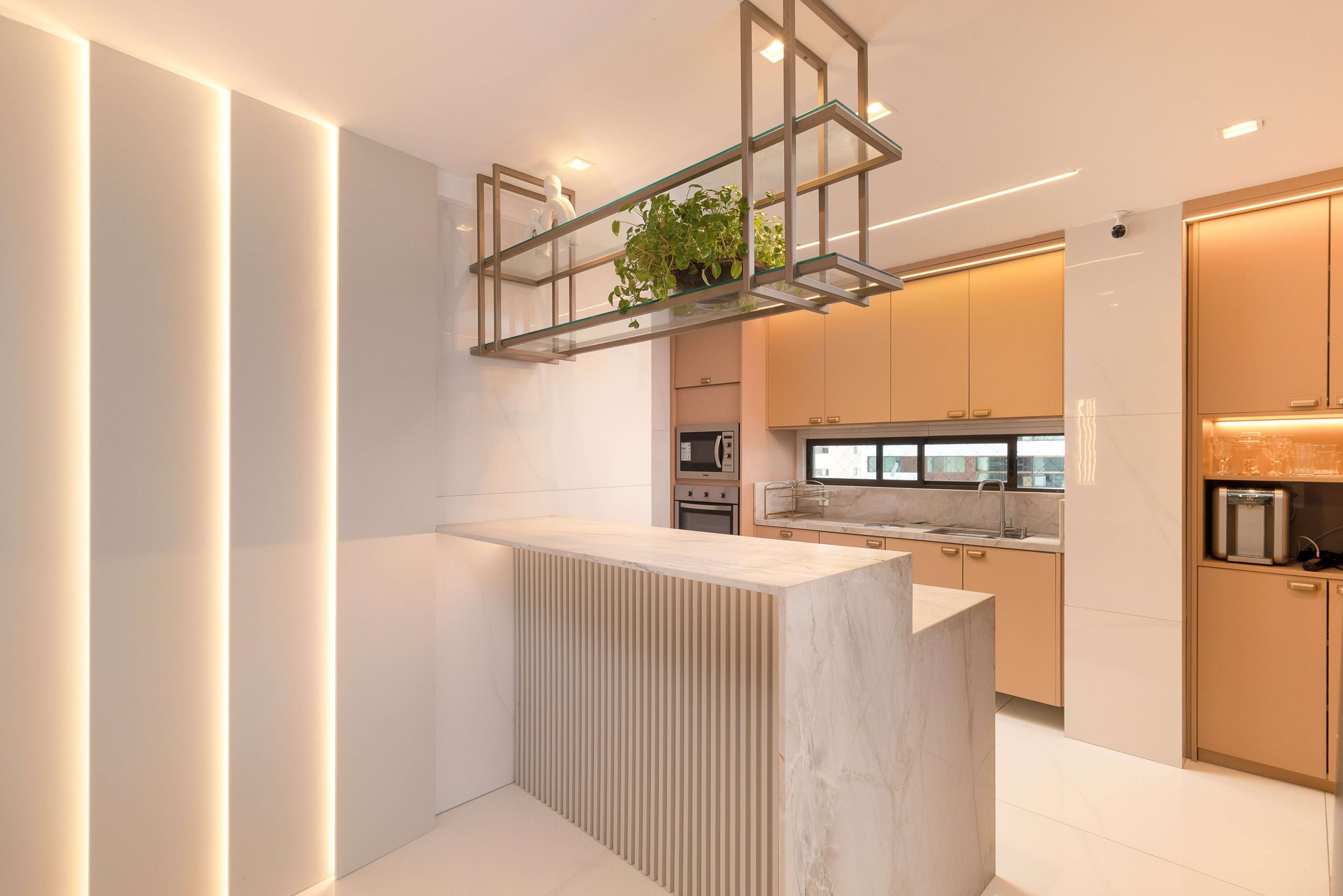 ambiente de cozinha integrado ao living. Ambiente em tom de pêssego levemente rosado (padrão DORT). Composição delicada e elegante. metais em tom champagne. iluminação embutida