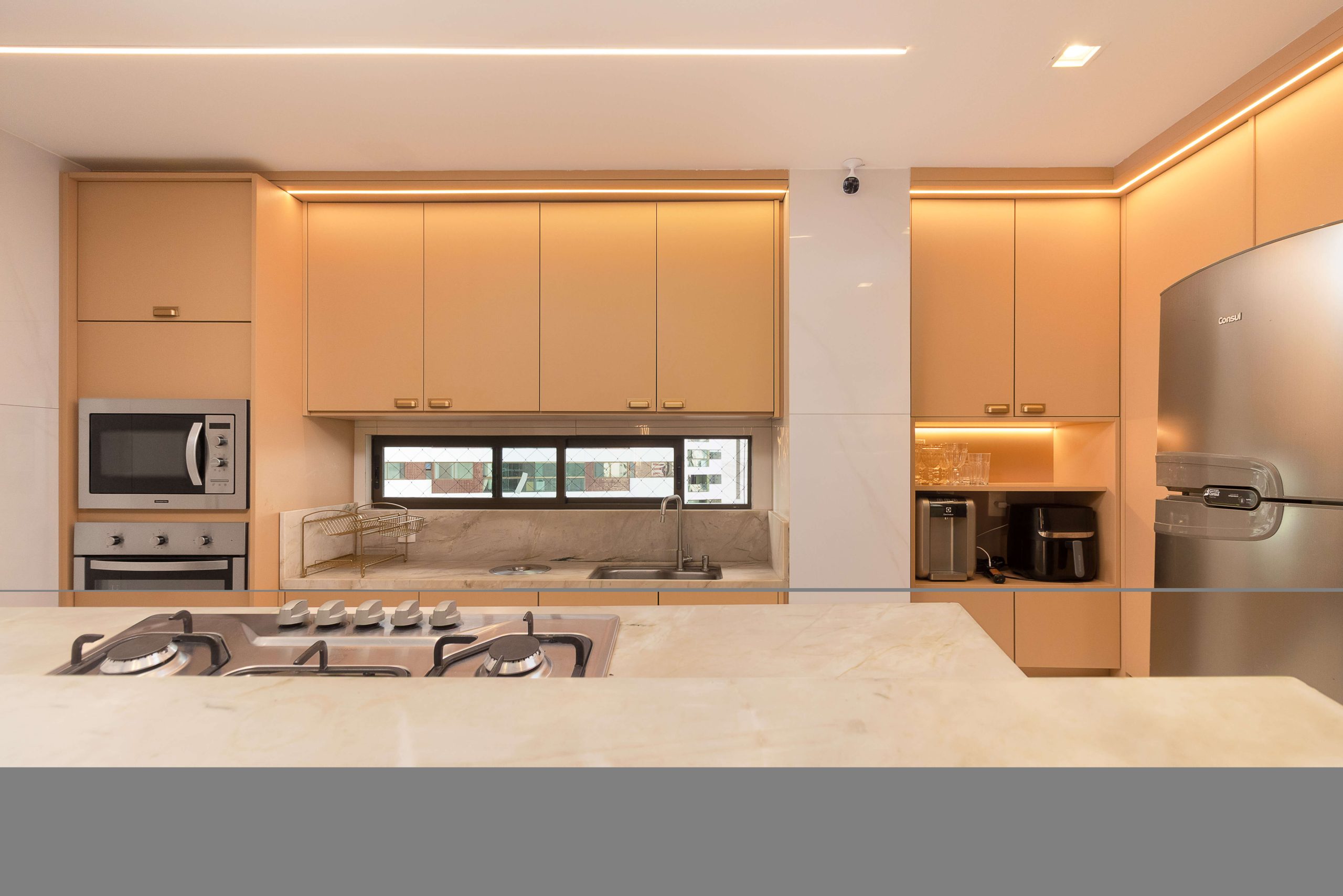 ambiente de cozinha integrado ao living. Ambiente em tom de pêssego levemente rosado (padrão DORT). Composição delicada e elegante. metais em tom champagne.