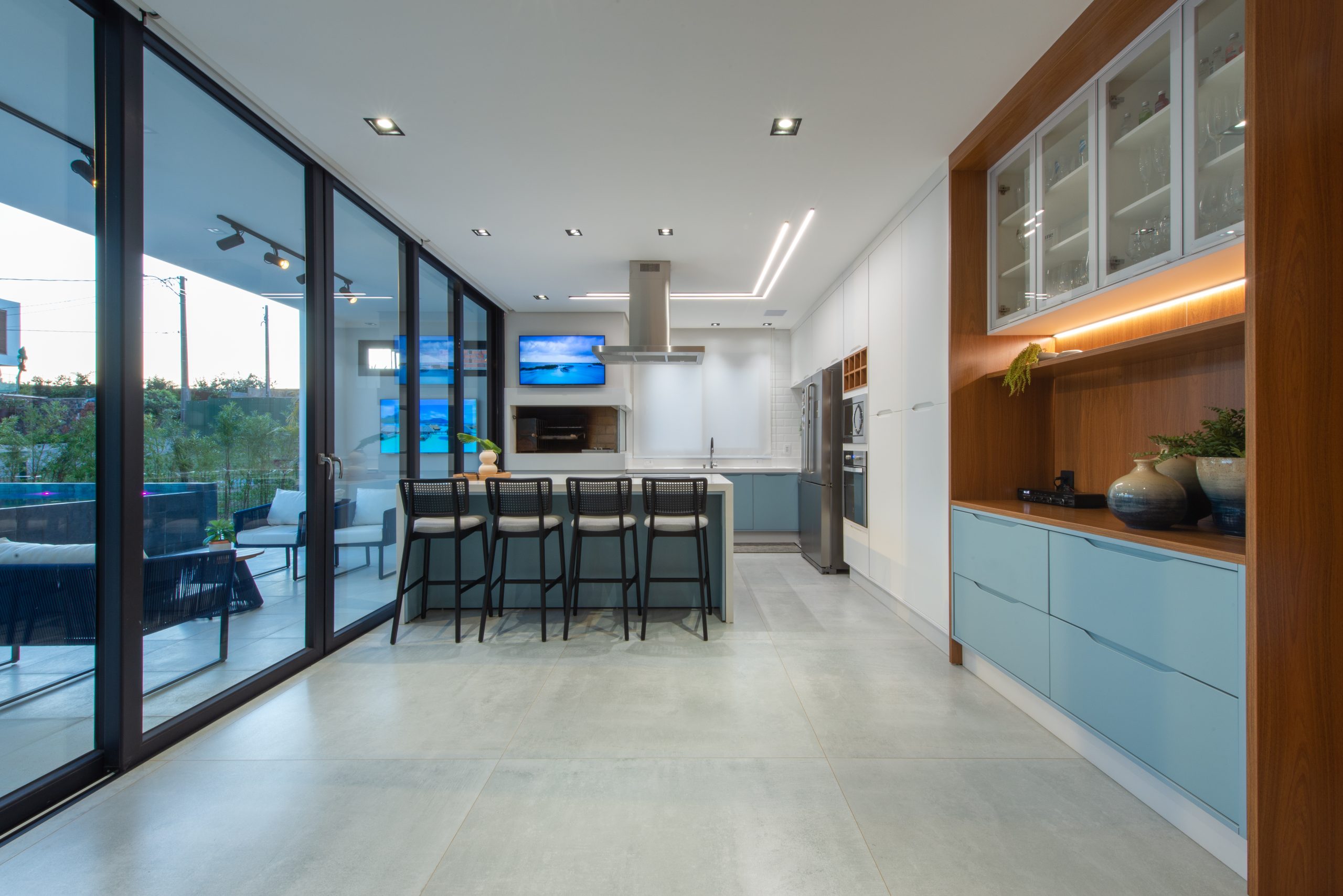 Cozinha Gourmet com acesso pra área externa em azul claro indigo (dusk) com branco e madeira Freijó. Cozinha com ilha ampla