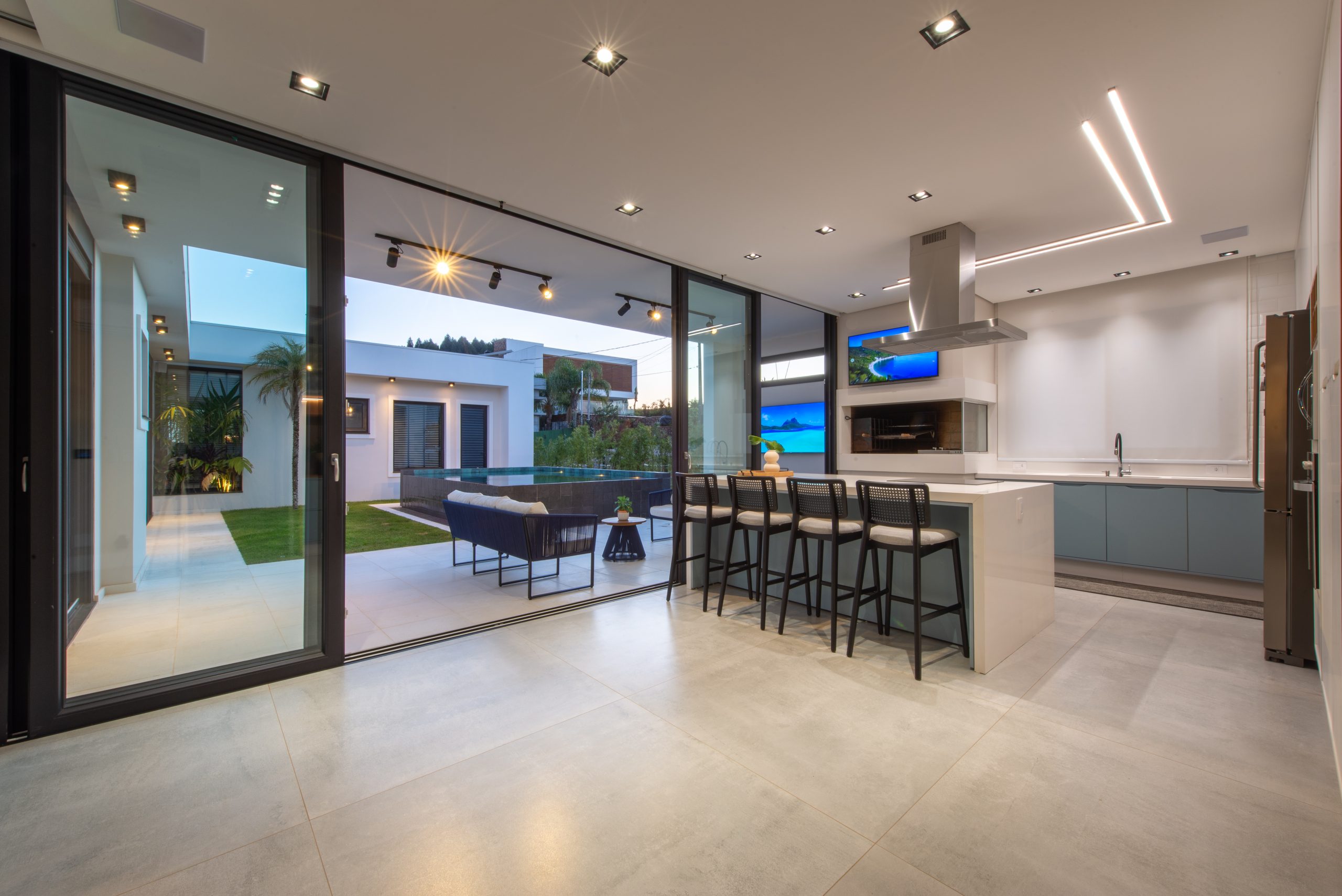 Cozinha Gourmet com acesso pra área externa em azul claro indigo (dusk) com branco e madeira Freijó. Cozinha com ilha ampla