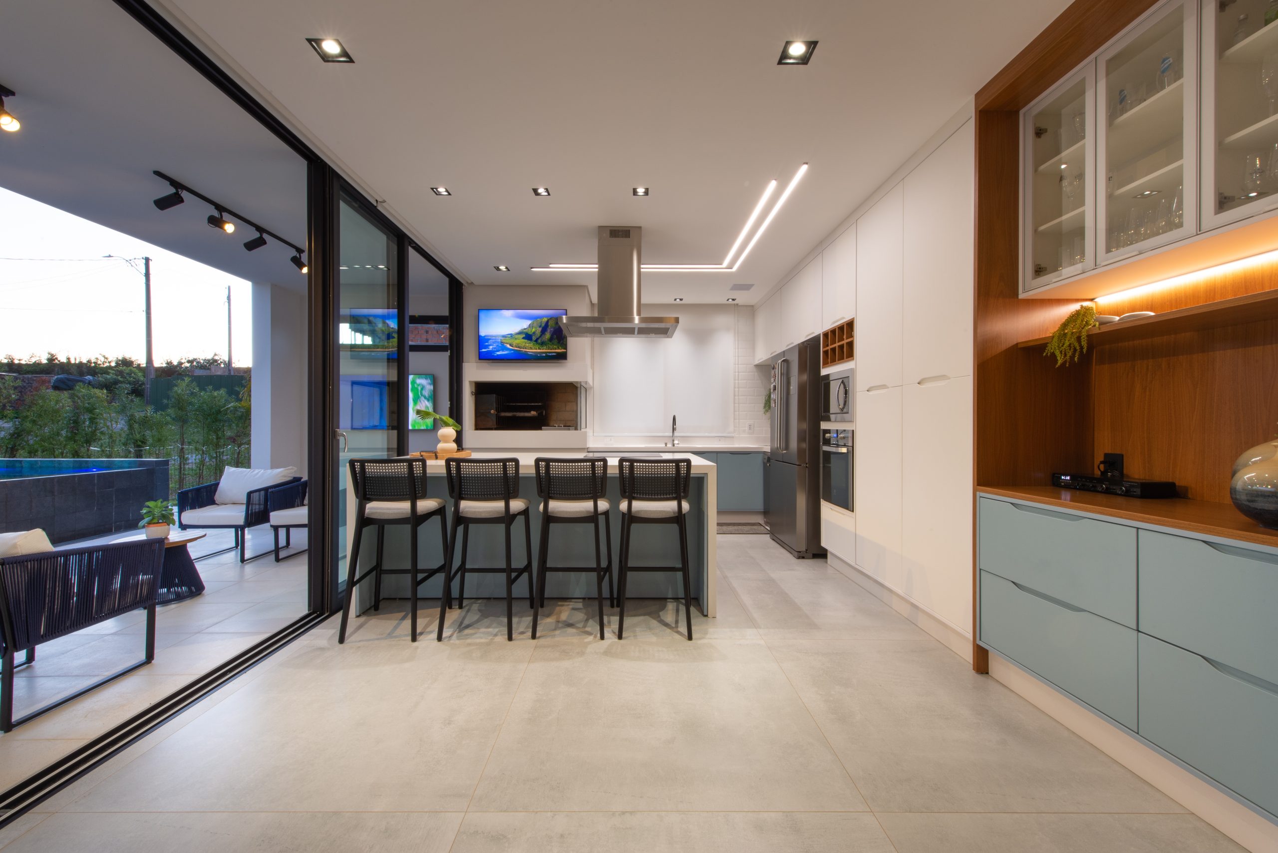 Cozinha Gourmet com acesso pra área externa em azul claro indigo (dusk) com branco e madeira Freijó. Cozinha com ilha ampla