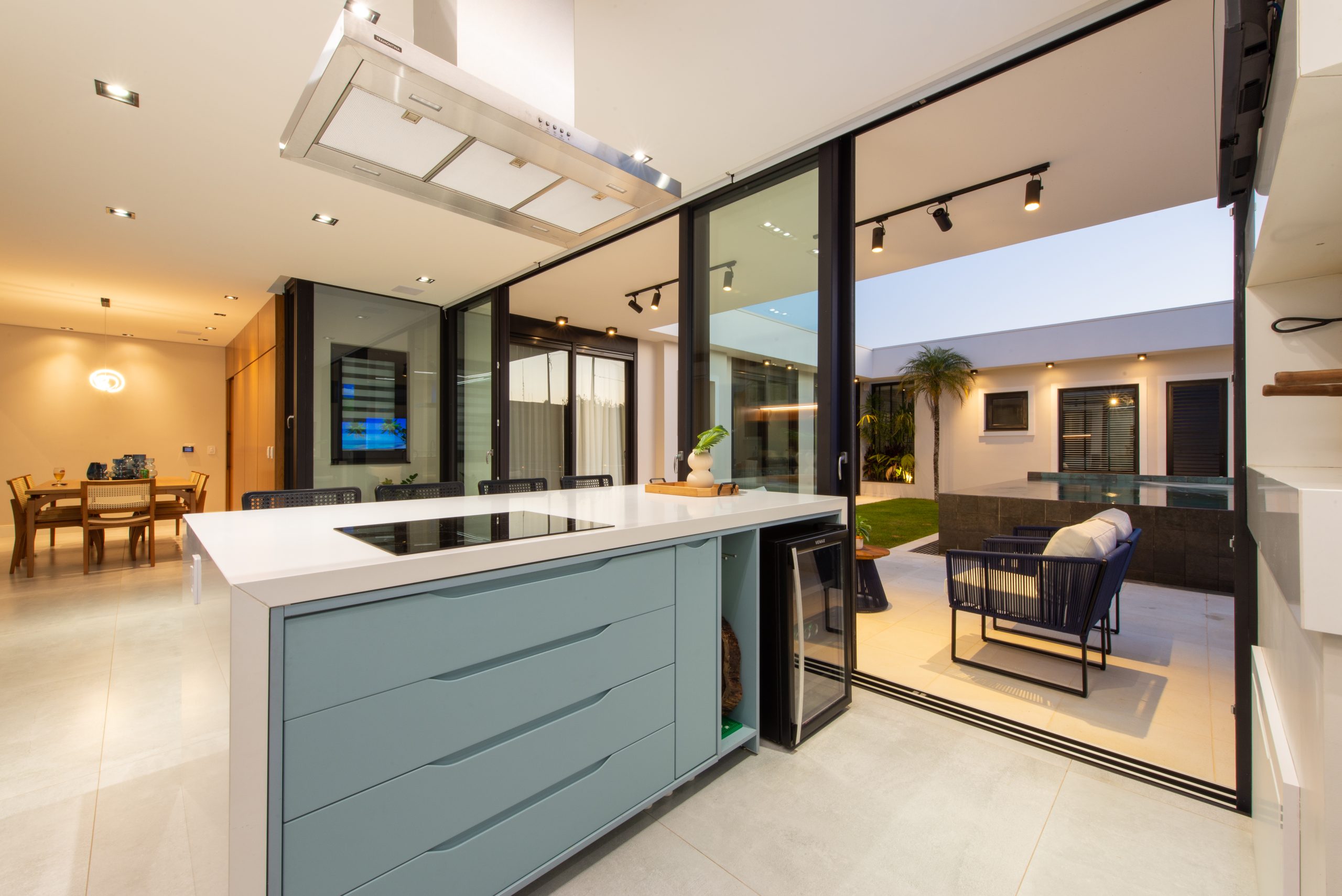 Cozinha Gourmet com acesso pra área externa em azul claro indigo (dusk) com branco e madeira Freijó. Cozinha com ilha ampla