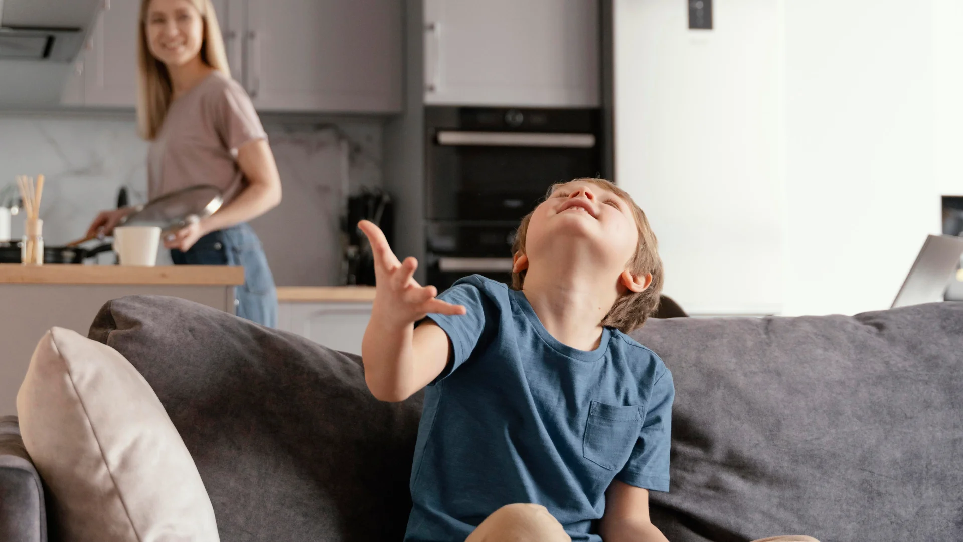 Conceito de ambientes integrados: menino brinca na sala enquanto mãe prepara refeição em cozinha com móveis sob medida em tons neutros.