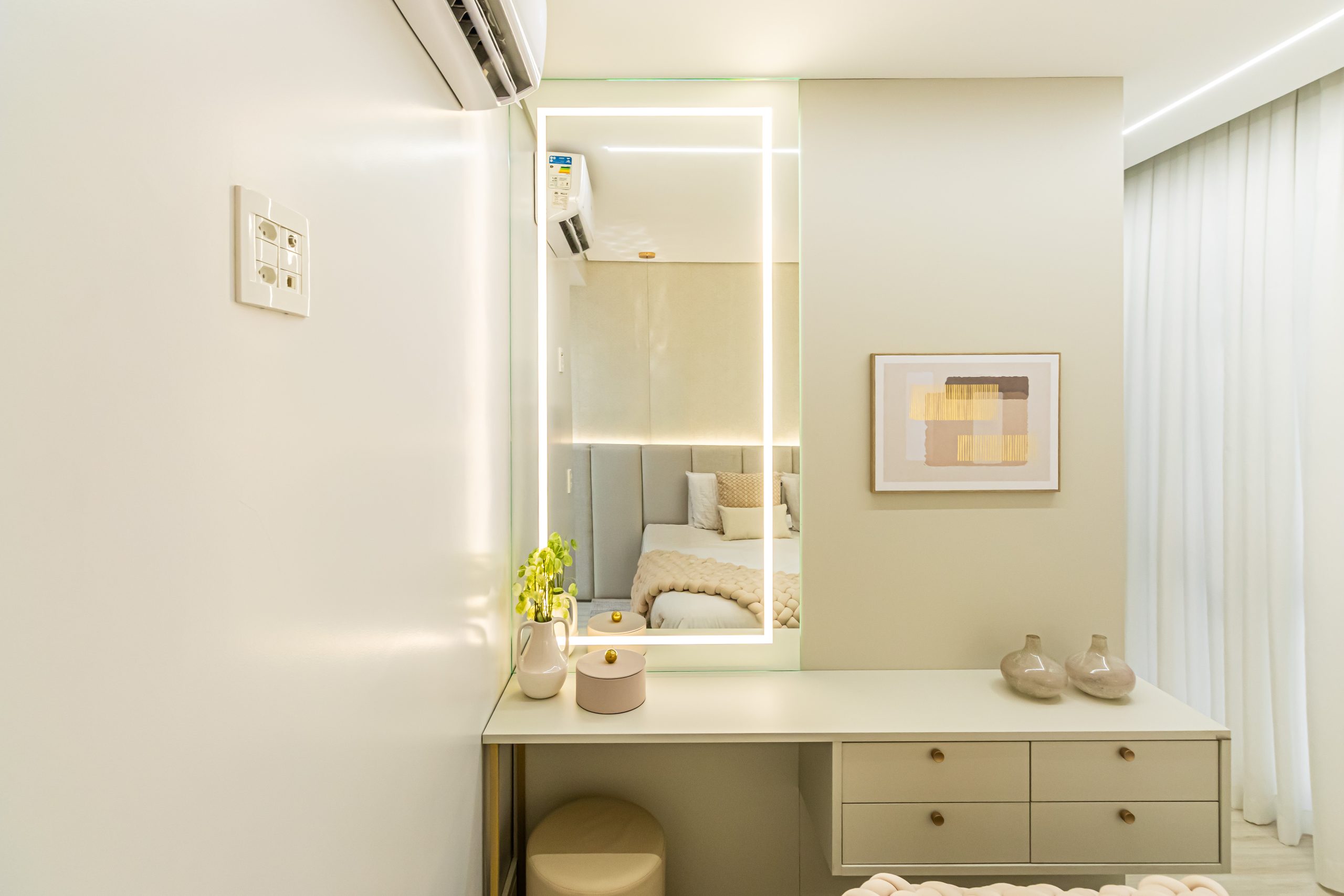 Suíte em tons claros de bege e areia com penteadeira compacta com espelho iluminado.