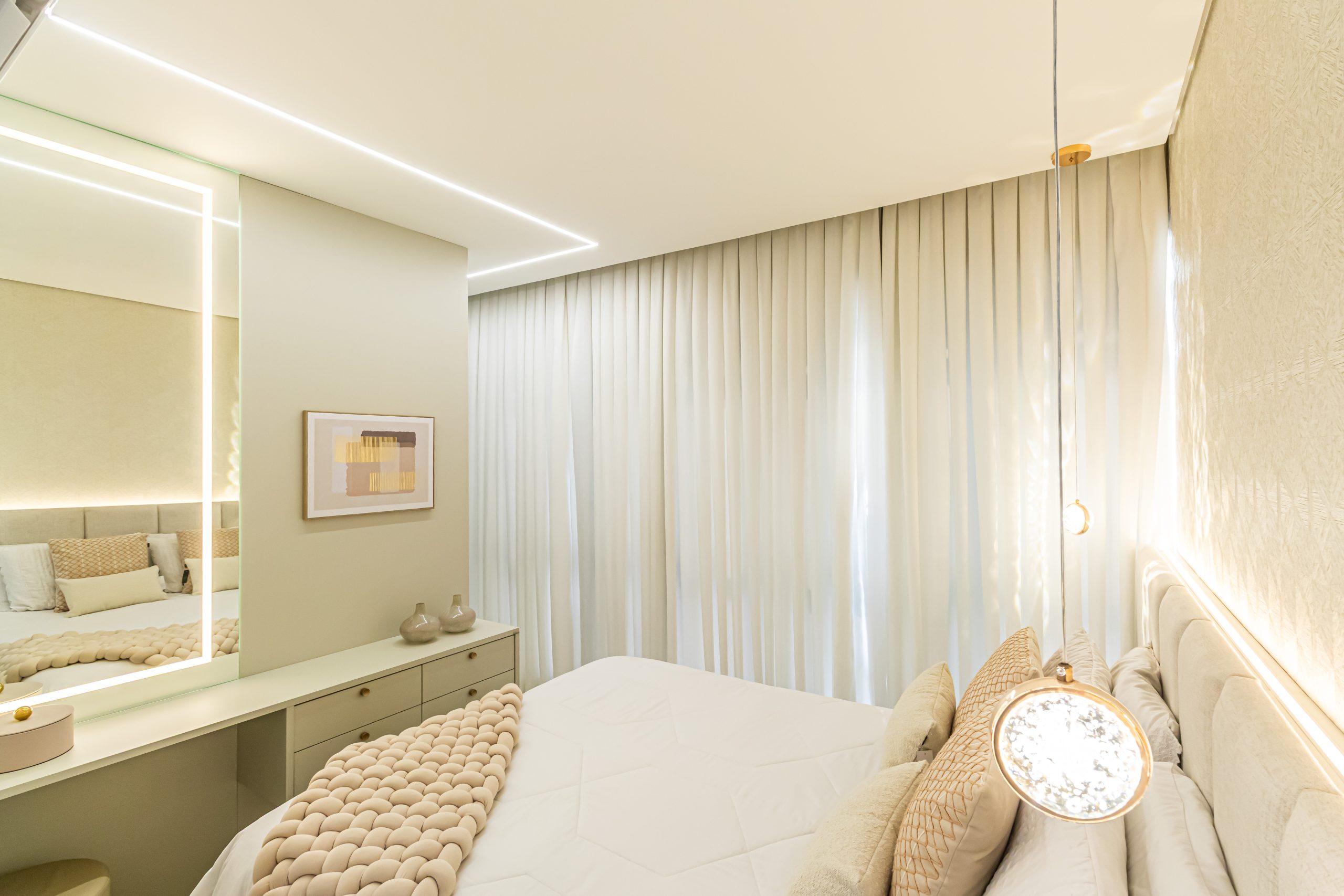 Suíte em tons claros de bege e areia com penteadeira compacta com espelho iluminado.