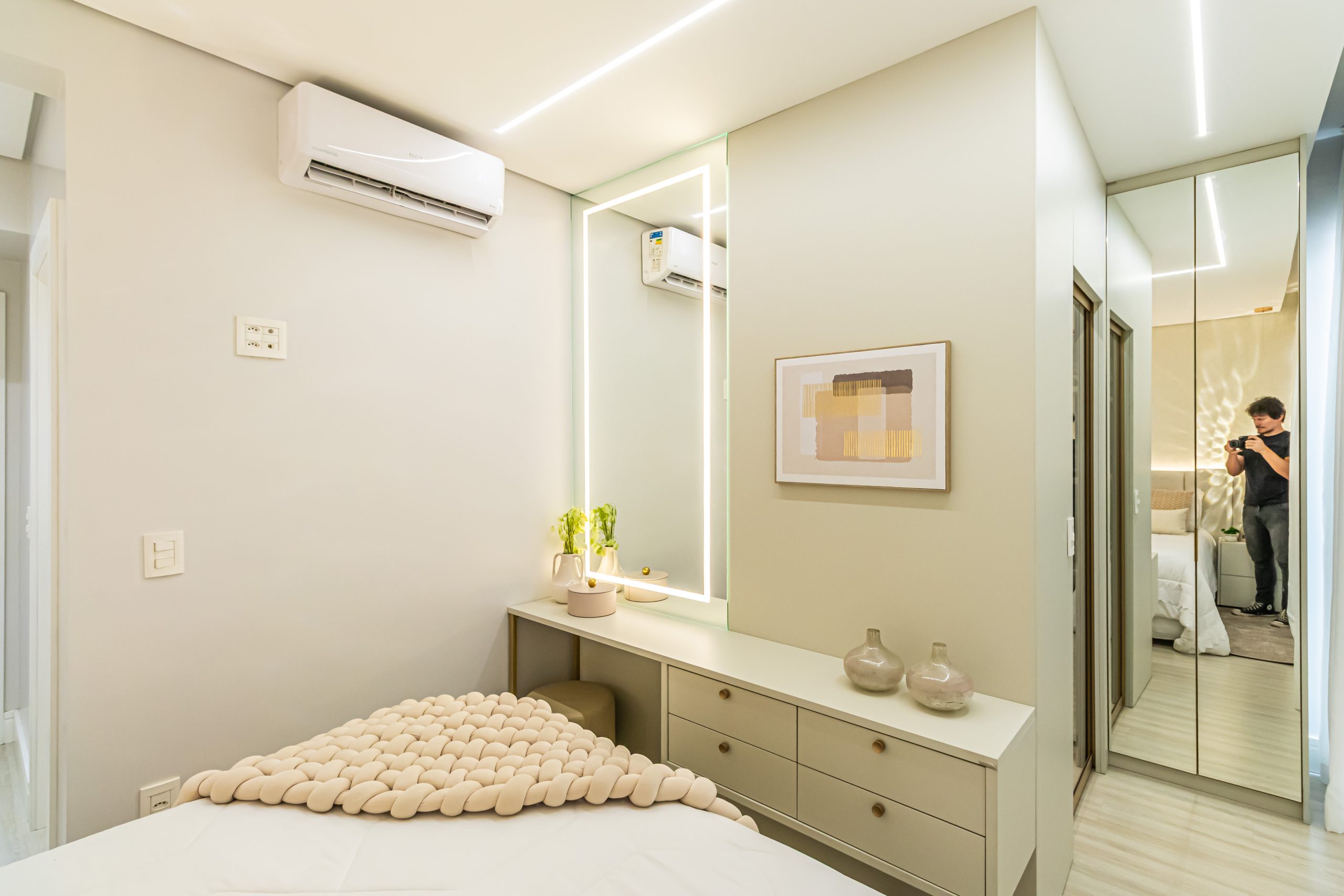 Suíte em tons claros de bege e areia com penteadeira compacta com espelho iluminado.