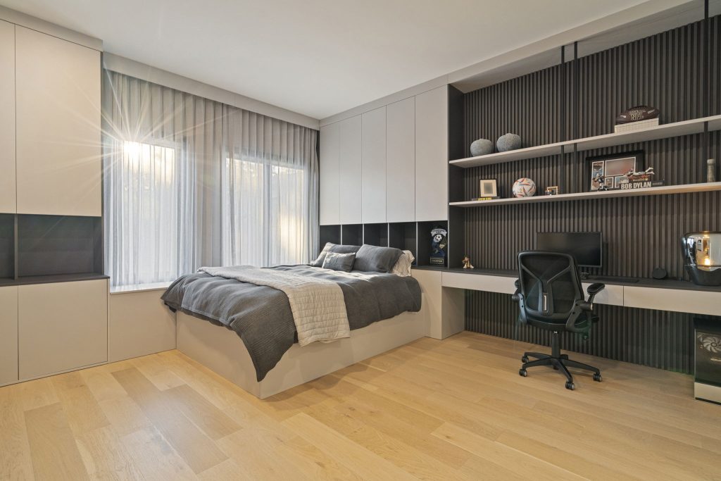 Dormitório de Casal com espaço de home office, com ripado na parede, composição do projeto em tons sóbrios: cinza médio com cinza claro. Projeto estilo mais minimalista sem puxador.