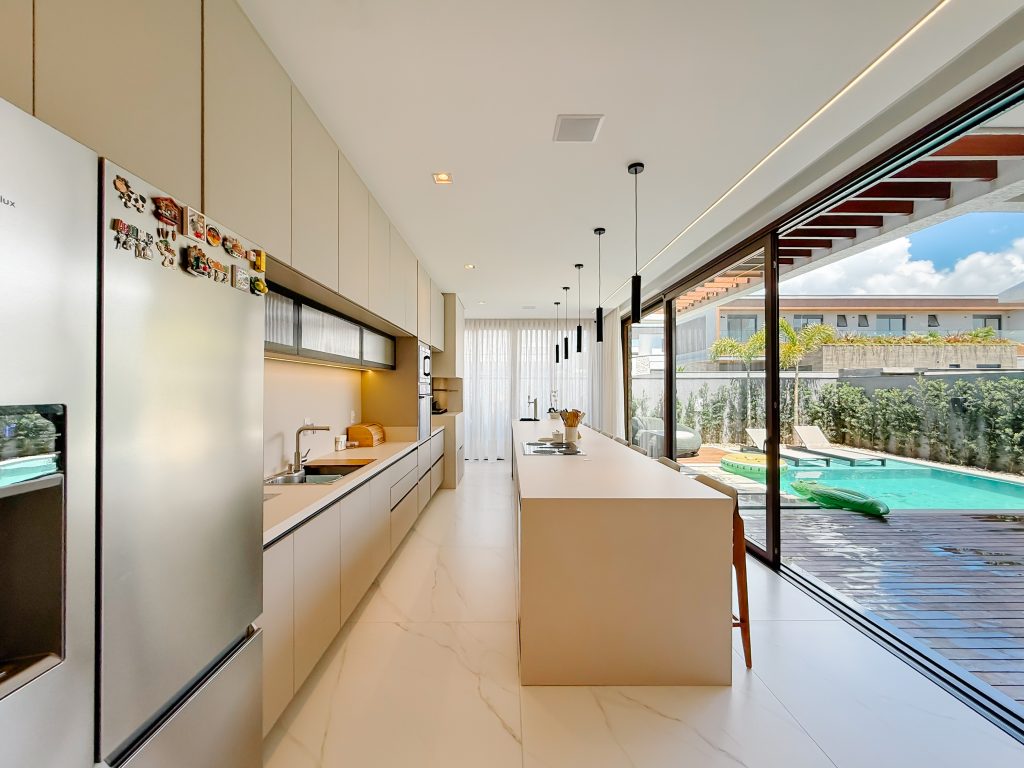 Gabinete de cozinha - cozinha aberta em tons claros com ilha integrada a área externa com piscina.